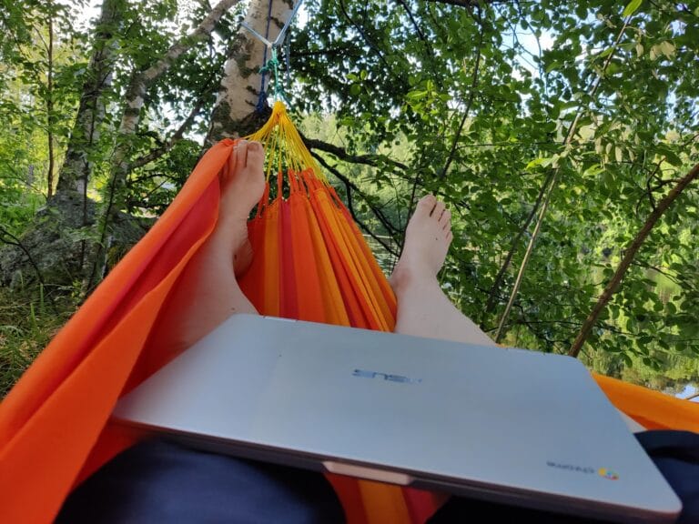 Kuvassa näkyy riippumatossa makaavan ihmisen jalat ja sylissä Chromebook